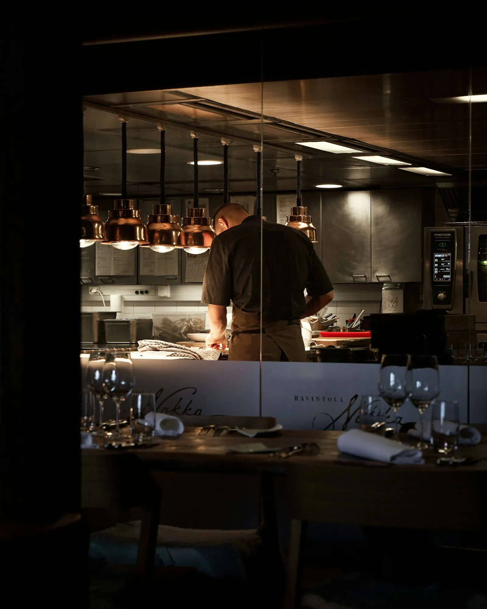 A chef working at the pass, seen through the glass from the dining room